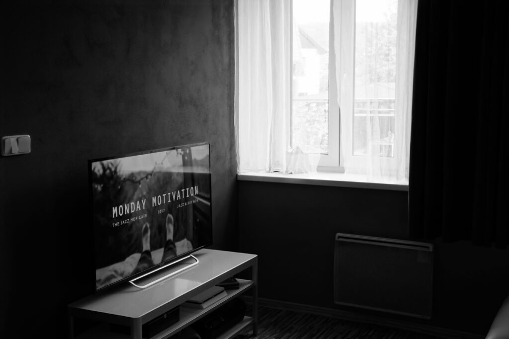 Black and white photo of a modern interior featuring a TV and window with sheer curtains.