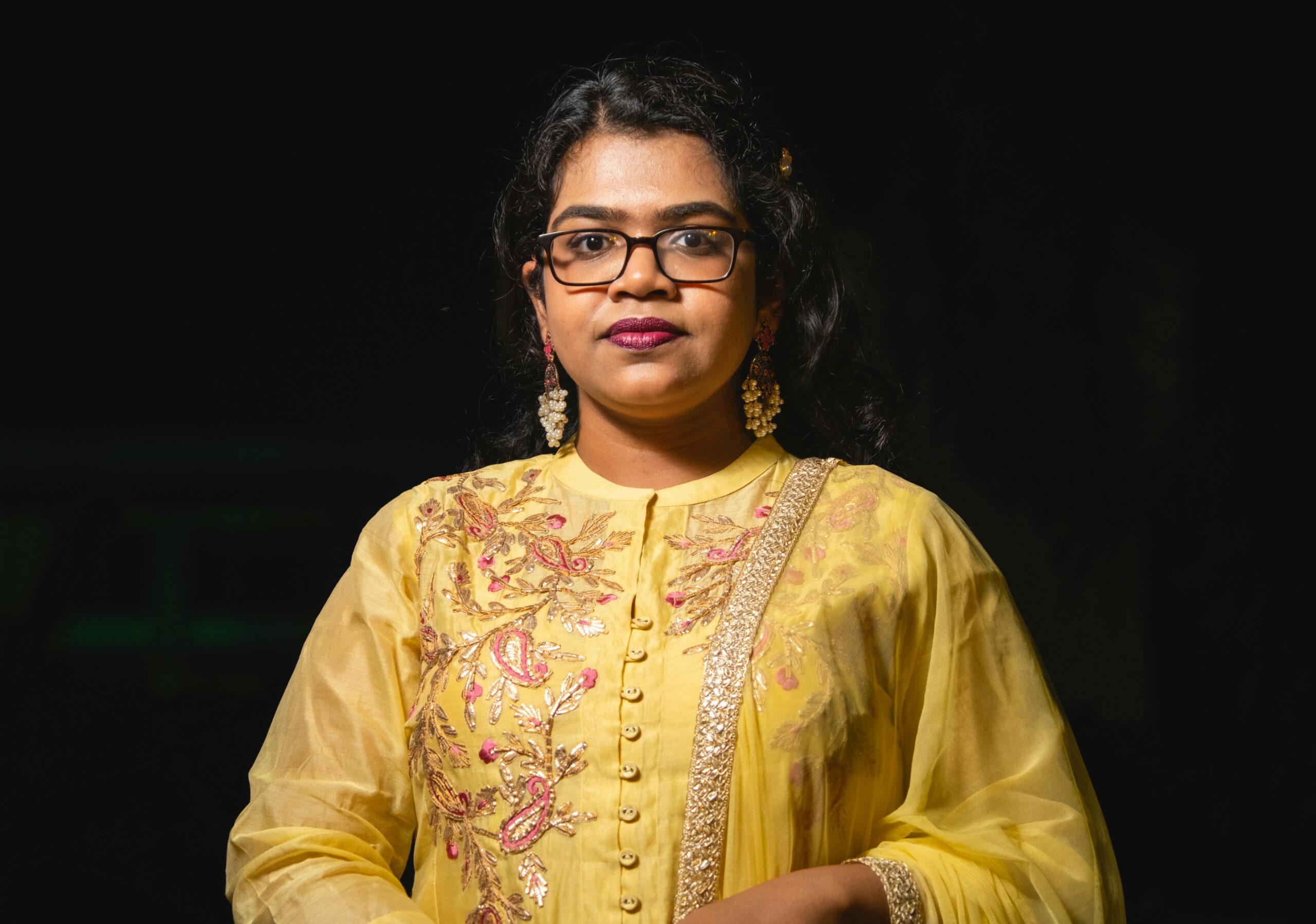 Stunning portrait of a woman in yellow traditional clothing with intricate embroidery and eyeglasses.