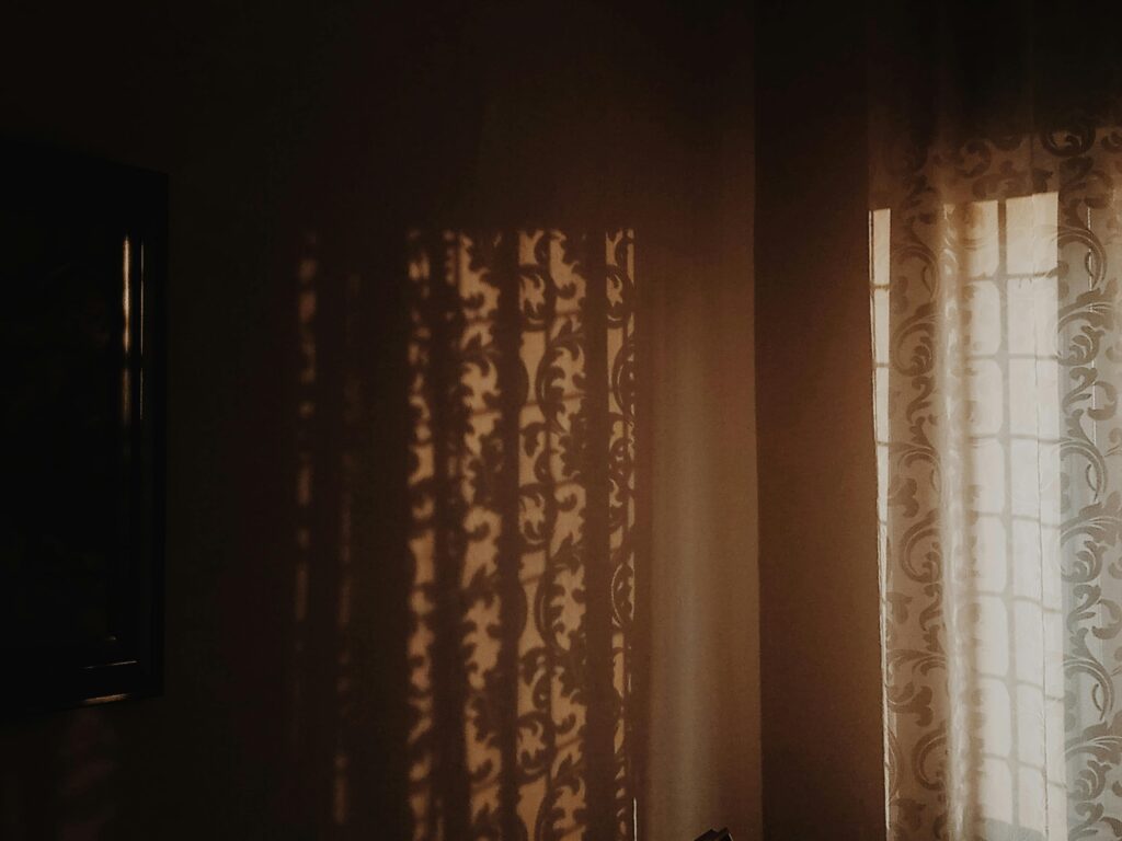 Warm sunlight casting intricate shadows through patterned curtains in a cozy indoor setting.
